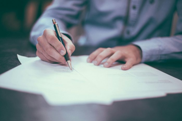 The image shows a person signing a document with a pen. This could be a high-net-worth individual signing their divorce papers. Choosing the right divorce solicitor is crucial for high-net-worth individuals due to the complex financial and legal implications involved. The image represents the importance of seeking expert legal advice to navigate the intricacies of such a divorce and ensure a fair settlement.