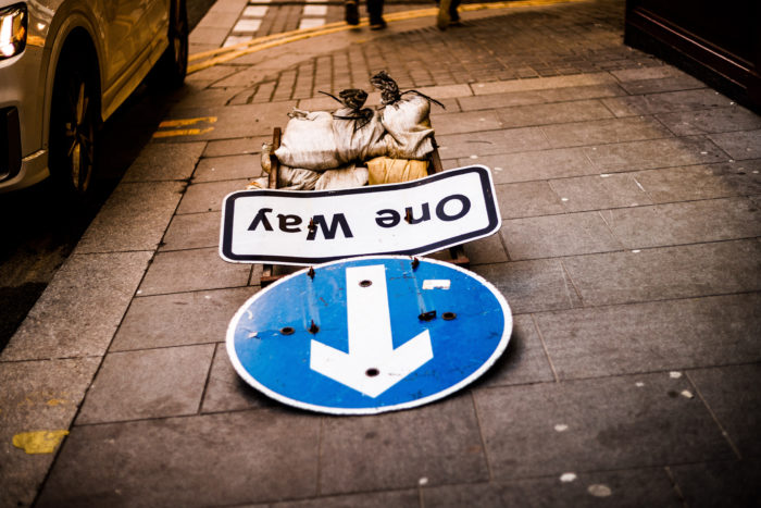 Upside-down 'One Way' sign and blue arrow pointing down on a city sidewalk, symbolising the crossroads in divorce decisions between mediation and litigation.