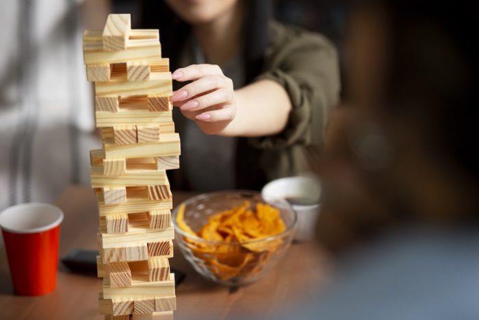A woman's hand carefully pulls a block from a tall wooden tower game, illustrating the need for a steady and precise approach to avoid mistakes during a financial settlement